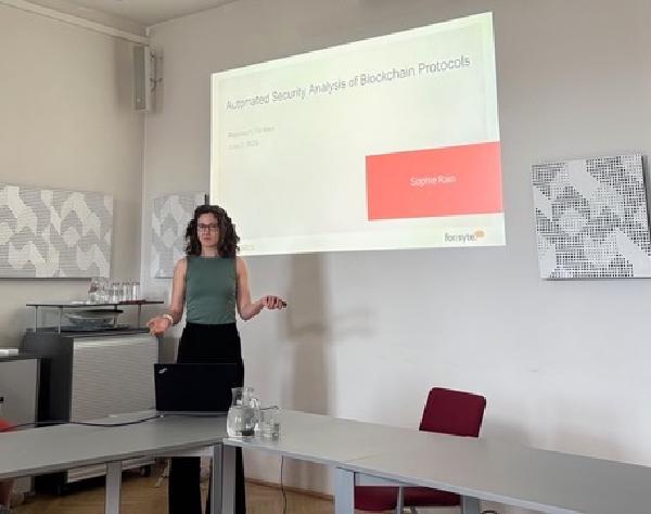 Sophie Rain stands in a seminar room delivering her PhD defense presentation. A slide displaying her name, the title, and the date is projected on the wall behind her.