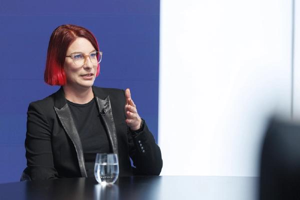 Prof. Martina Lindorfer, wearing glasses and a black blazer, speaks and gestures during an interview, seated at a table.