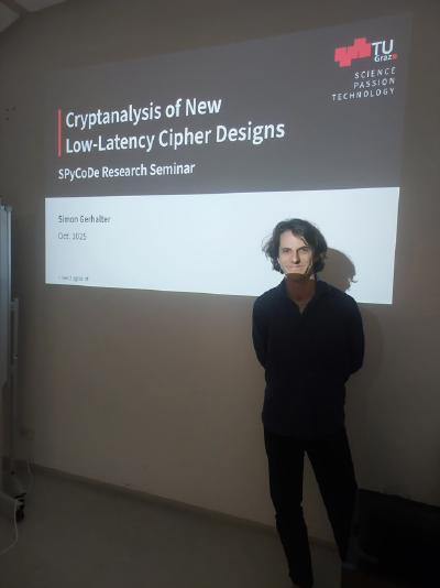 Simon Gerhalter stands beside a projected slide titled “Cryptanalysis of New Low-Latency Cipher Designs” with TU Graz logo visible. Simon Gerhalter stands beside a projected slide titled “Cryptanalysis of New Low-Latency Cipher Designs” with TU Graz logo visible.