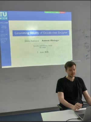 Andreas Weninger seats at a desk in a classroom, giving a presentation. Behind him is a projection screen displaying a slide titled 'Committing Security of Encode-then-Encipher'