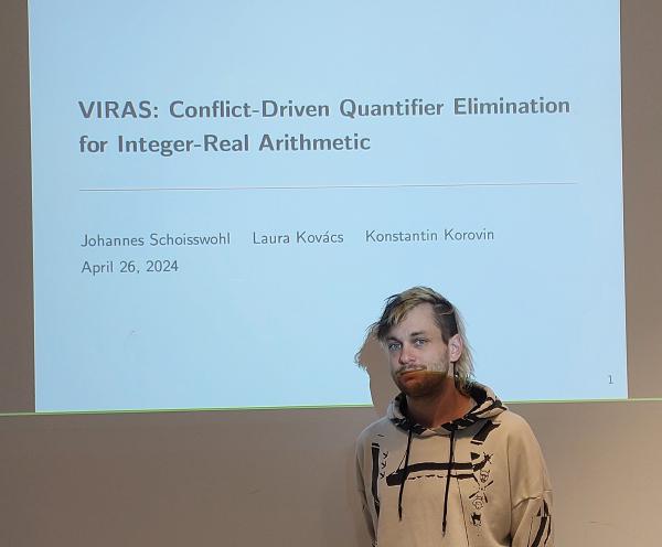 Johannes Schoisswohl is standing before the screen. On the screen the first slide of the presentation is displayed