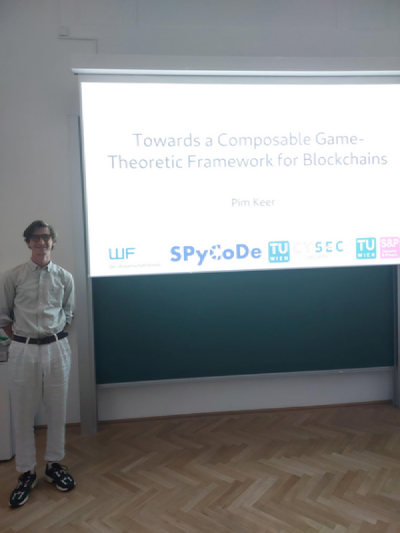 Research seminar presentation by Pim Keer on a composable game-theoretic framework for blockchains. The slide includes the logos of FWF, SPyCoDe, TU Wien, CYSEC, and TU Wien Security & Privacy. A small video call window on the right shows the lecture room with the presenter standing at the front. Research seminar presentation by Pim Keer on a composable game-theoretic framework for blockchains. The slide includes the logos of FWF, SPyCoDe, TU Wien, CYSEC, and TU Wien Security & Privacy. A small video call window on the right shows the lecture room with the presenter standing at the front.
