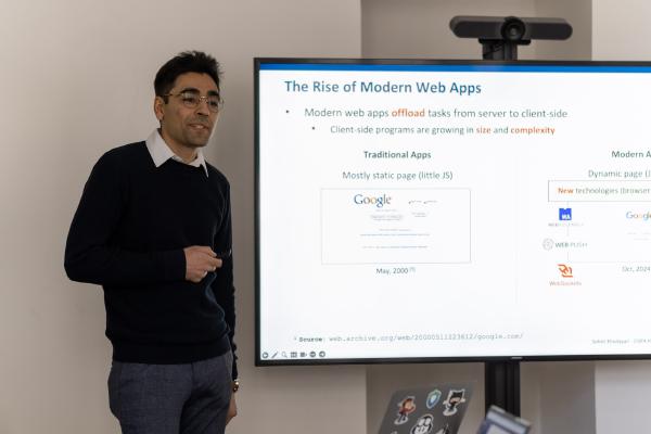 Photo of Soheil Khodayari standing next to the screen with a slide from his presentation.