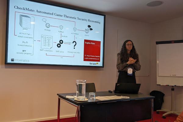 Sophie Rain  is giving a presentation at the conference. A slide from the presentation is displayed on the screen, showing the workflow diagram of CheckMate