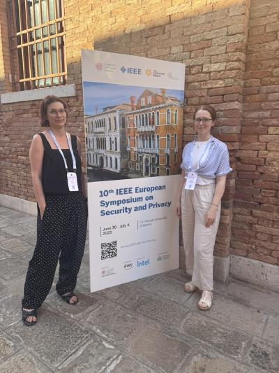 Martina Lindorfer and Magdalena Steinböck stand next to a large poster for the “10th IEEE European Symposium on Security and Privacy”