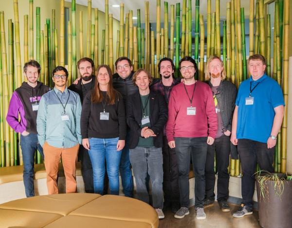 A group of nine individuals posing in a conference room. They are all wearing conference badges and are part of a professional or academic gathering. 